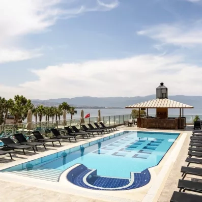 Une piscine extérieure bordée de transats, offrant une vue dégagée sur la mer et les montagnes.