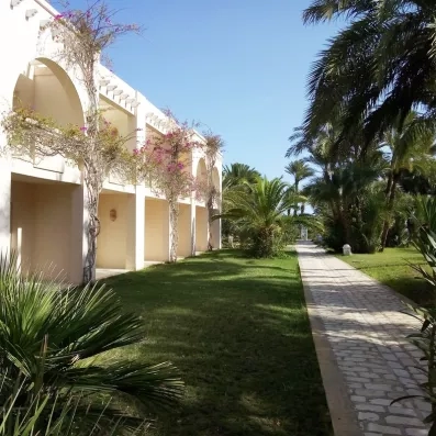 Allée pavée longeant les bâtiments des chambres de l'hôtel, agrémentée de bougainvilliers grimpants et de végétation méditerranéenne.