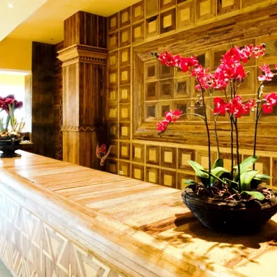 Comptoir de réception en bois sculpté avec motifs géométriques et décoration florale élégante (orchidées roses) à l'intérieur de l'hôtel.