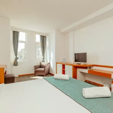 La chambre montrant un lit double, un bureau en bois clair et une fenêtre offrant une vue dégagée.