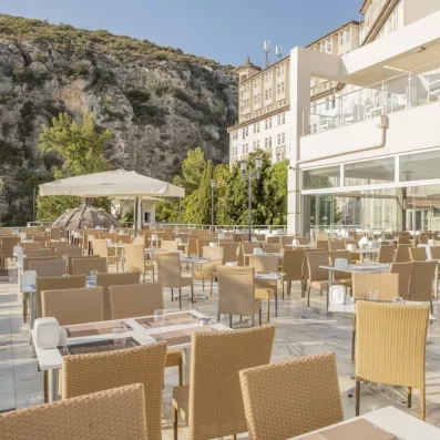 Une vaste terrasse ensoleillée bordée par une falaise, aménagée avec des tables en plein air.