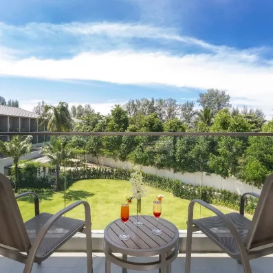 Un balcon avec une table et deux chaises, offrant une vue face à un jardin.