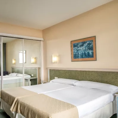 Une chambre d'hôtel sobre et lumineuse avec un grand lit double et un miroir mural.