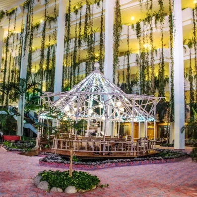 Un bar de jardin intérieur abrité sous une structure en verre et entouré de végétation.