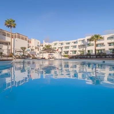 Une grande piscine aux eaux cristalline avec des palmiers d'un complexe hôtelier sous un ciel bleu.