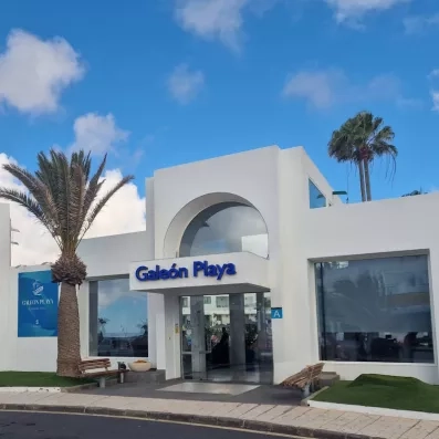La façade blanche et moderne de l'établissement, sous un ciel bleu parsemé de palmiers.