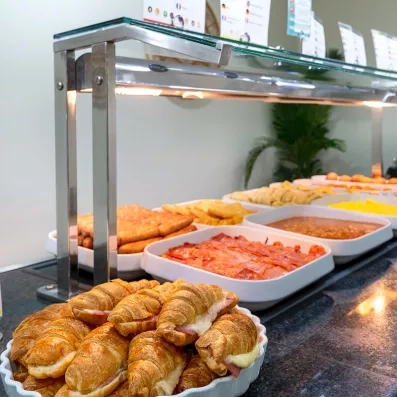 Un buffet de plats chauds et de viennoiseries présenté sous des lampes chauffantes.
