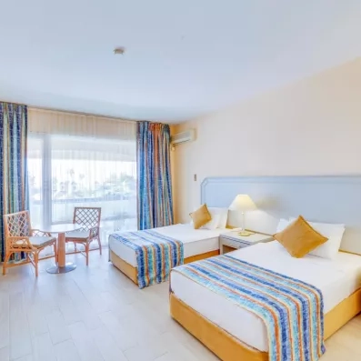 Une chambre lumineuse avec deux lits simples et un petit coin salon près de la fenêtre.