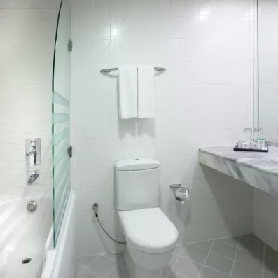 Une salle de bain, comprenant une baignoire avec paroi vitrée et un toilette.