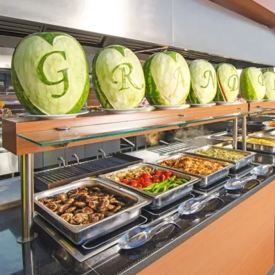 Un long buffet de plats chauds surmonté de pastèques sculptées au-dessus.