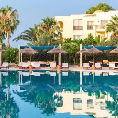 Grande piscine bordée de palmiers, transats ombragés et hôtel en arrière‑plan