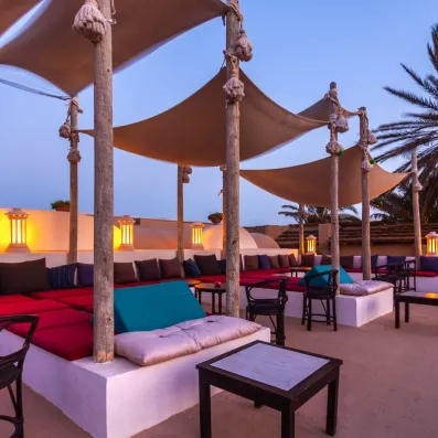 Espace lounge extérieur aux coussins colorés, éclairé par lanternes chaleureuses