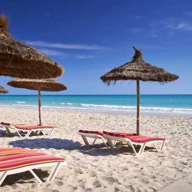 Plage de sable fin, eaux turquoise et parasols en paille typiques de l'hôtel Les Quatre Saisons.