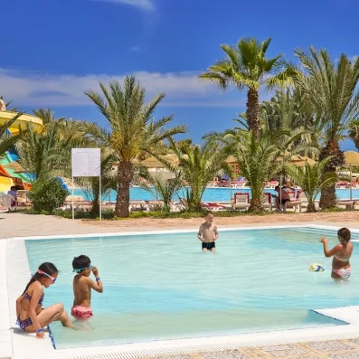 Enfants s'amusant dans le pataugeoire de l'hôtel Les Quatre Saisons sous les palmiers.