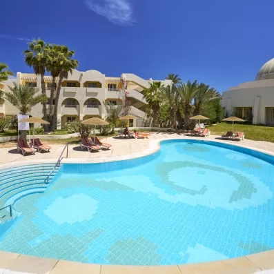 Piscine extérieure entourée de transats et architecture tunisienne traditionnelle aux Quatre Saisons à Djerba.