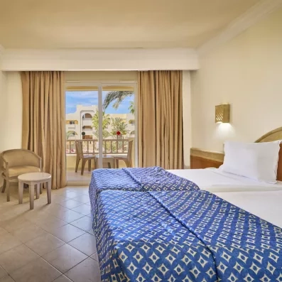 Chambre lumineuse avec balcon vue sur piscine et palmiers à l'hôtel Les Quatre Saisons à Djerba, Tunisie.