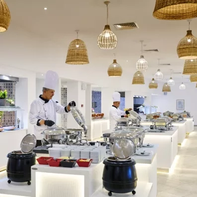 Chefs cuisiniers préparant des plats chauds en buffet sous des luminaires en osier à Djerba.