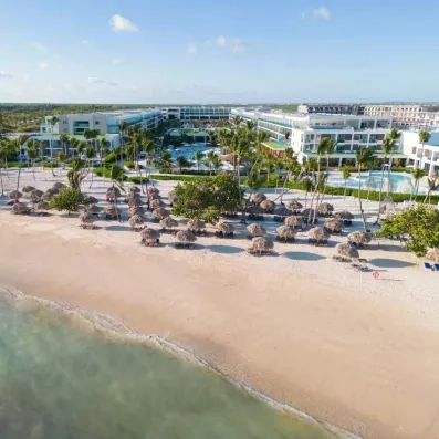 vue aérienne de la plage de sable, et de l'hôtel avec ses piscines, palmiers, transats et avents paillote