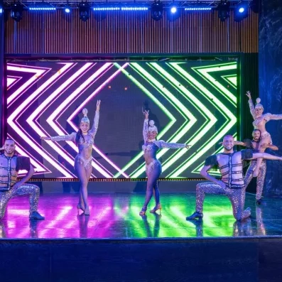 spectacle avec des danseurs habillés en tenue de carnaval, lumières vertes et roses derrière eux