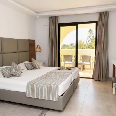 Chambre d'hôtel spacieuse avec balcon privé offrant une vue sur les jardins palmiers du Djerba Aqua Resort.