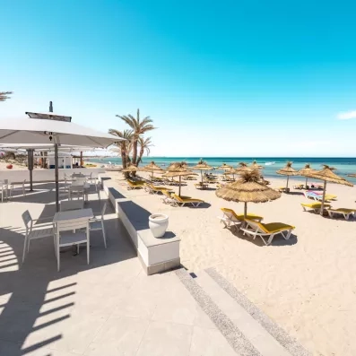 Plage de sable fin aménagée avec transats et parasols traditionnels sous le soleil de Djerba.