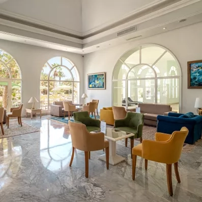 Lobby d'hôtel luxueux à Djerba avec mobilier coloré, sol en marbre et grandes baies vitrées lumineuses.