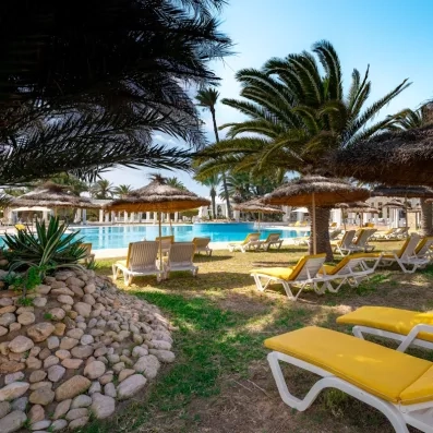 Grande piscine extérieure bordée de transats jaunes et de parasols en paille sous le soleil de Djerba.