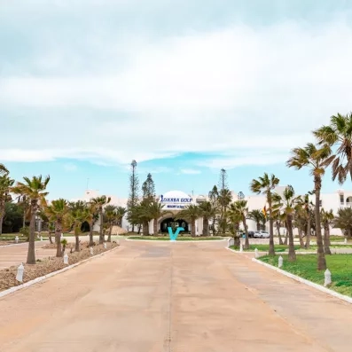 Allée principale bordée de palmiers menant à l'entrée de l'hôtel Djerba Golf Resort & Spa en Tunisie.
