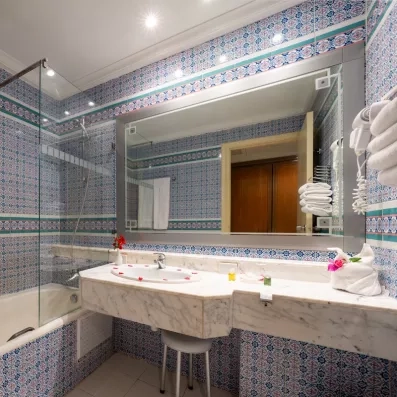 Salle de bain typique à l'hôtel Djerba Golf avec carrelage mosaïque bleu, marbre et baignoire moderne.