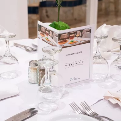 Menu du restaurant Il Gusto posé sur une nappe blanche avec verres et couverts à Djerba.