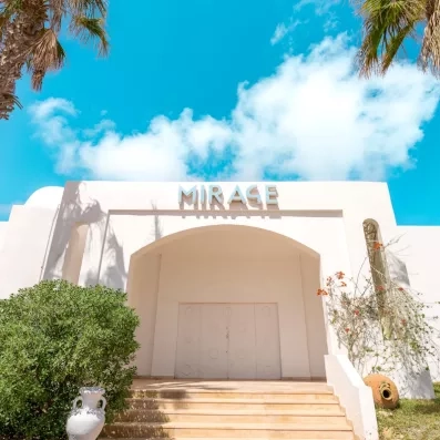 Façade blanche épurée de l'espace Mirage sous un ciel bleu radieux à l'hôtel Djerba Golf Resort.