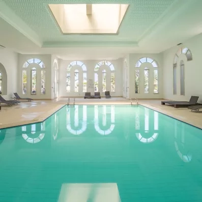 Piscine intérieure chauffée baignée de lumière naturelle avec larges baies vitrées donnant sur les jardins tunisiens.