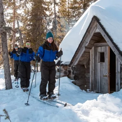 Trois skieurs avancent en file près cabane enneigée forêt calme