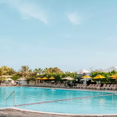 Grande piscine extérieure du Djerba Aqua Resort bordée de parasols jaunes et transats sous un ciel azur.
