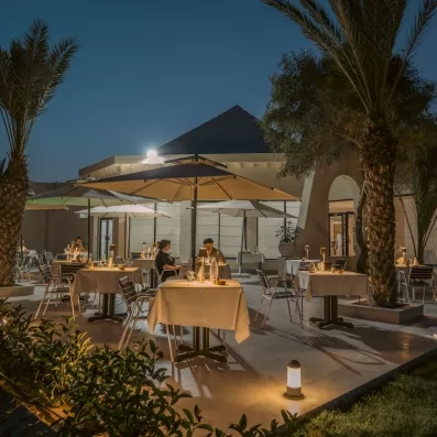 Terrasse de restaurant en plein air avec parasols et palmiers pour un dîner romantique à Djerba.