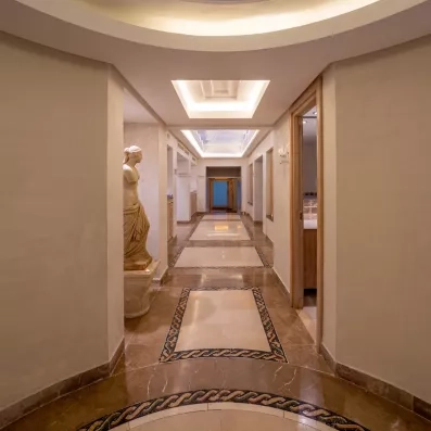 Couloir luxueux du spa de l'hôtel Djerba Golf avec statues antiques et sol en mosaïque raffinée.