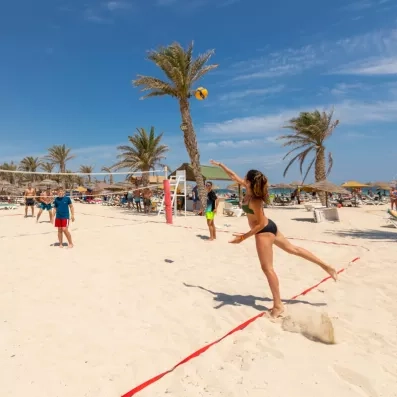 Match de beach-volley sur plage ensoleillée avec joueuse servant et palmiers.