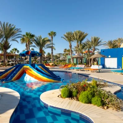 Parc aquatique avec toboggans colorés, piscine et palmiers dans un cadre tropical ensoleillé.