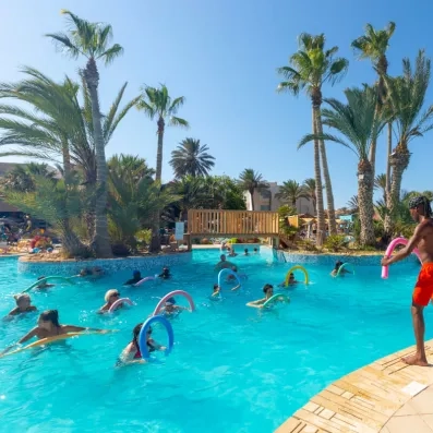 Séance d’aquagym dans piscine de resort avec participants et palmiers en arrière-plan.