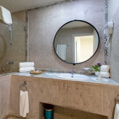 Salle de bain élégante avec grand miroir rond, lavabo en marbre, baignoire et accessoires soigneusement disposés.