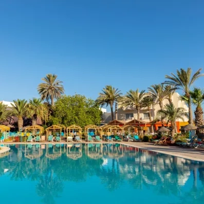 Piscine extérieure turquoise entourée de cabanas jaunes, transats bleus et palmiers sous un ciel ensoleillé.