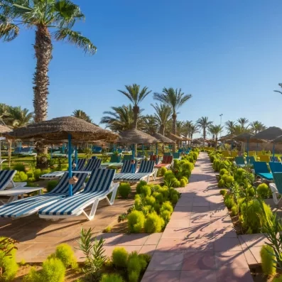 Rangées de transats rayés sous parasols en chaume dans un jardin tropical ensoleillé.