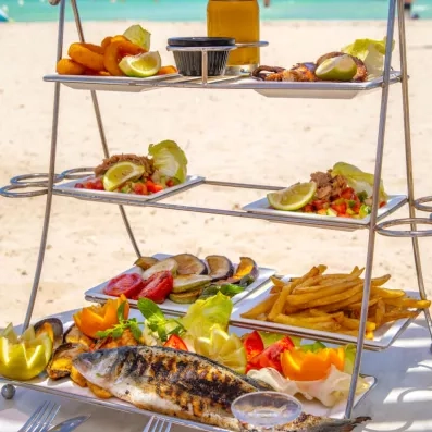 Plateau de fruits de mer servi en étages face à la plage, avec poisson grillé, salades et calamars.
