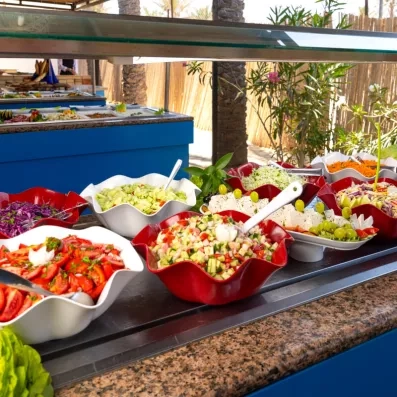 Buffet de salades fraîches en plein air avec légumes variés, fruits et plats colorés présentés dans des bols décoratifs dans une ambiance tropicale.