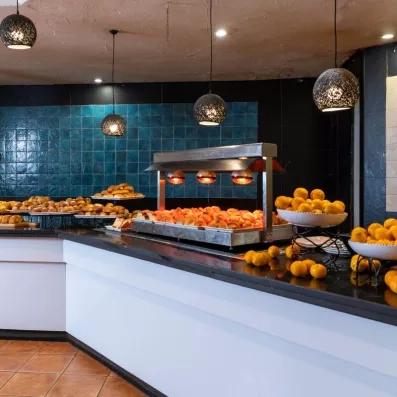 Buffet de viennoiseries avec croissants, pains, fruits frais et lampes chauffantes.
