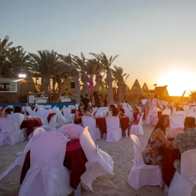 Dîner sur la plage avec tables décorées, invités et ambiance dorée au coucher du soleil.