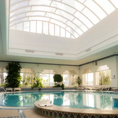 Piscine intérieure chauffée sous verrière lumineuse avec chaises longues au One Resort Aqua Park à Monastir.
