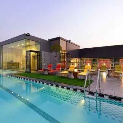 La piscine s'illumine face à un bâtiment moderne aux larges baies vitrées.