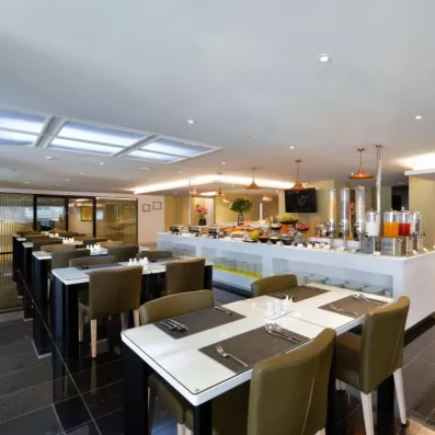 Une vue de la salle de restaurant moderne, montrant des tables dressées et le buffet au fond.