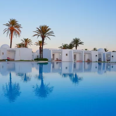 Grande piscine bleue reflétant les bungalows blancs et les palmiers du One Resort Aqua Park à Monastir.